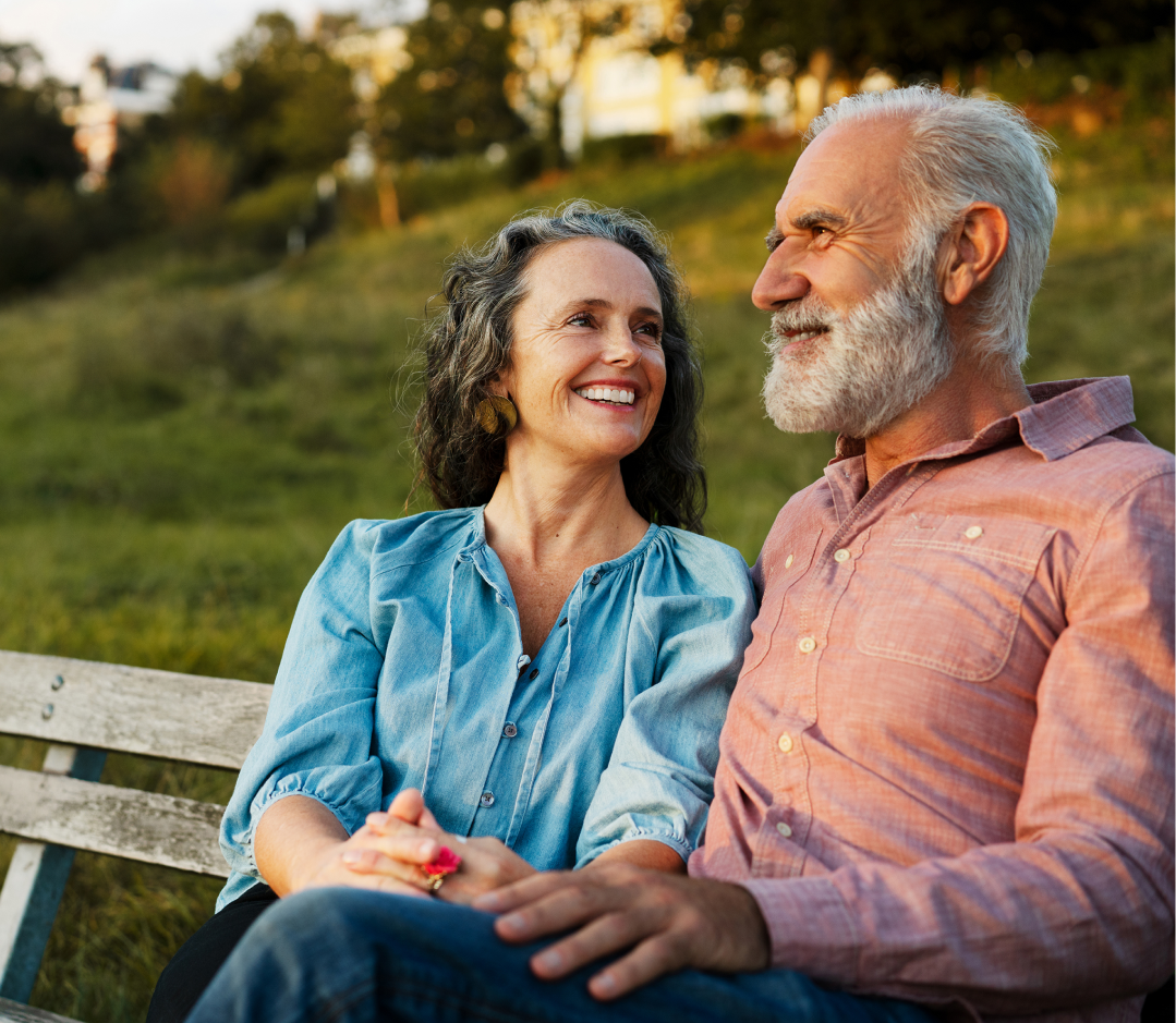 A man and woman smile and talk on a bench outside