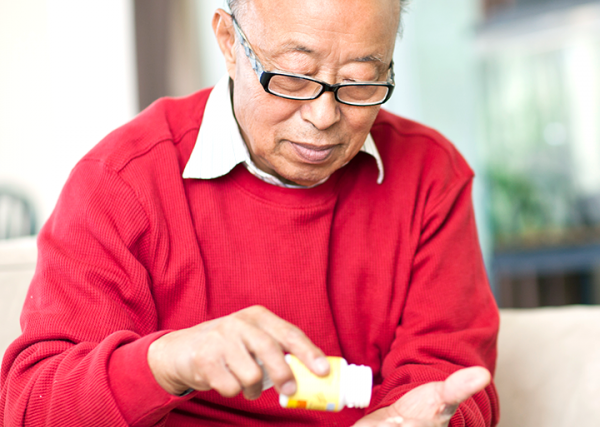 An older man empties a pill into his hand from a medication bottle.