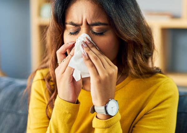 A young woman with allergies sneezes into a tissue.