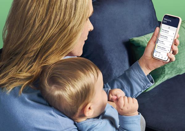 A woman uses the Express Scripts® Pharmacy app on her mobile phone while sitting with her baby on her lap.