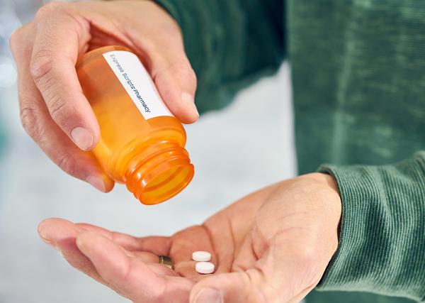 A man pours the last two pills from a prescription bottle into his hand.