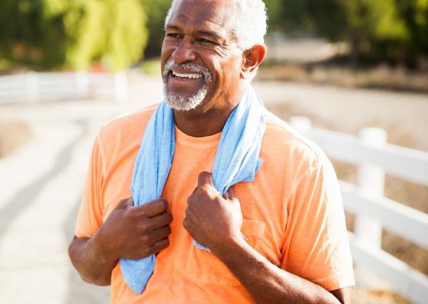 A man smiles in the sun with a small towel around his neck after enjoying some exercise outside.