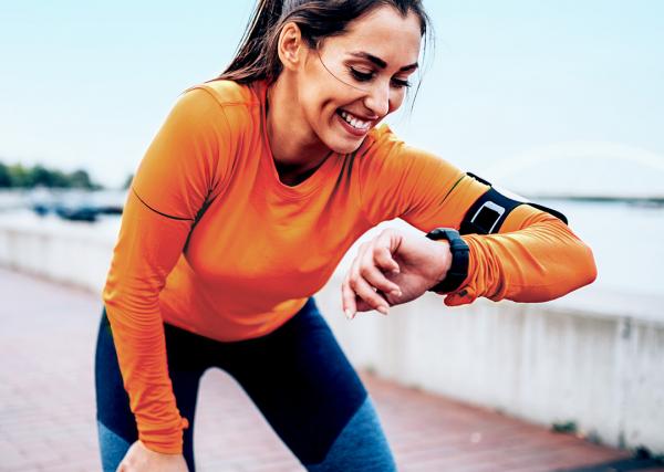 A woman takes a break while going for a run to check her smartwatch.