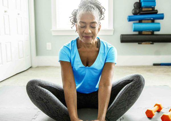A woman meditates on an exercise mat at home.