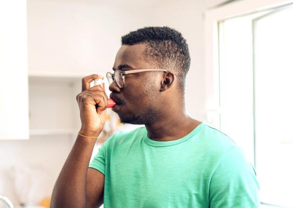 A young man uses his inhaler in his kitchen.