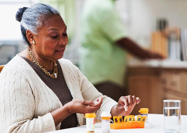 An older woman sorts her medication doses into a weekly pill organizer.
