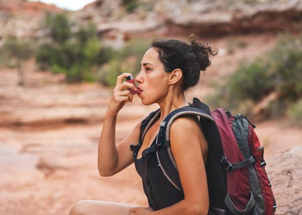 A young woman stops on a hike to use her rescue inhaler, which is an example of an as-needed medication.