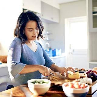 A young woman chops healthy ingredients on a cutting board in her kitchen.