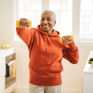 An older woman uses a pair of dumbbells to work out at home.