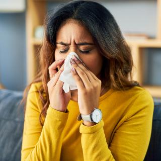 A young woman with allergies sneezes into a tissue.