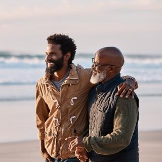 A young man and his father enjoy walking along the beach at sunset.