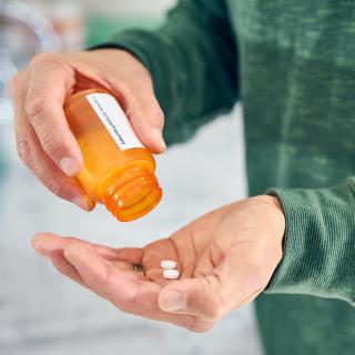 A man pours the last two pills from a prescription bottle into his hand.