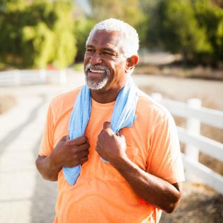 A man smiles in the sun with a small towel around his neck after enjoying some exercise outside.