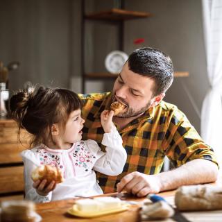 A toddler feeds her father a piece of her croissant.