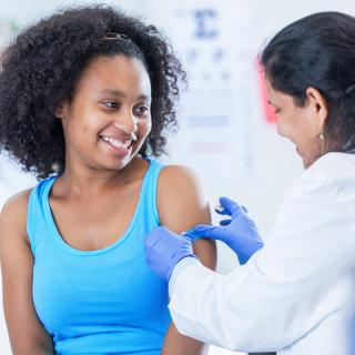 A teenage girl smiles after receiving a vaccine.