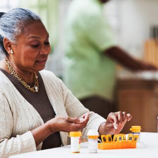 An older woman sorts her medication doses into a weekly pill organizer.