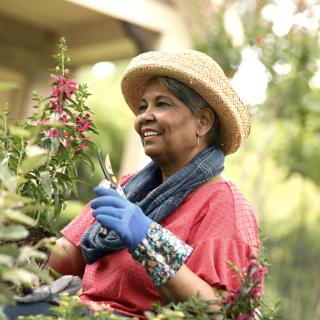 A older women smiles as she trims the flowers outside in her garden.