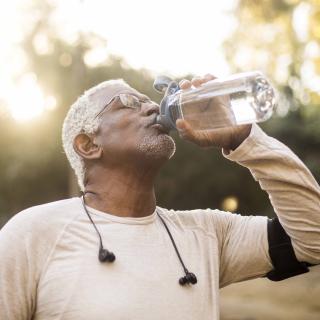 An older man takes a swig of water from his water bottle while enjoying the outdoors.