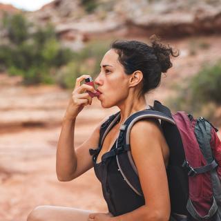 A young woman stops on a hike to use her rescue inhaler, which is an example of an as-needed medication.